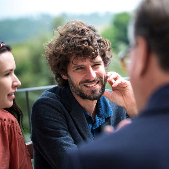A man with curly hair engaged in a phone conversation, expressing enthusiasm for joining Teva.